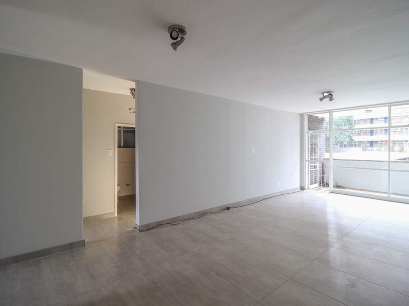 A bright, open-plan living area featuring neutral tiled flooring, modern track lighting, and a large glass sliding door leading to an outdoor space.