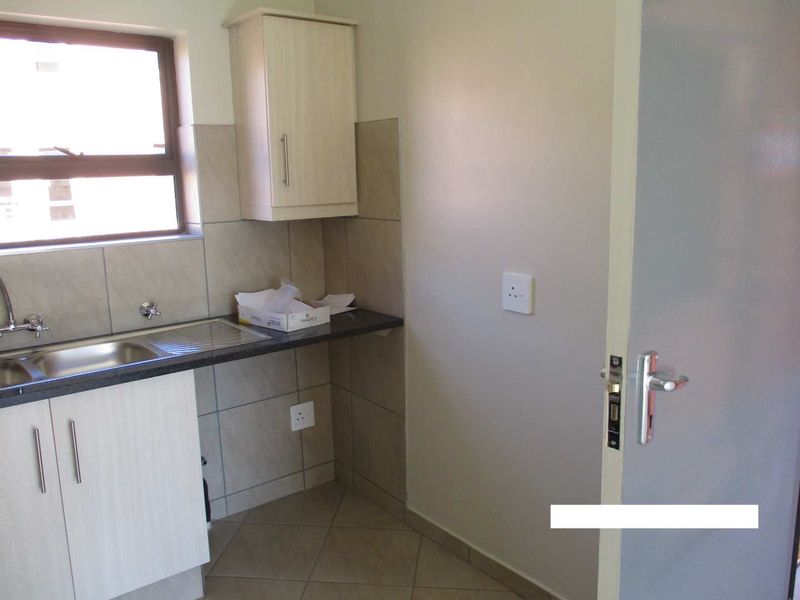 A compact and functional scullery area featuring built-in cabinetry, a stainless steel sink, granite countertops, and neutral tiled finishes.