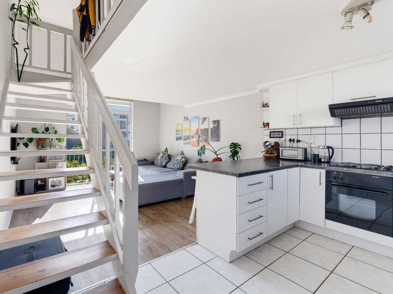 Open-plan living area featuring a modern kitchen with built-in appliances, tiled flooring, and a staircase leading to an upper level.