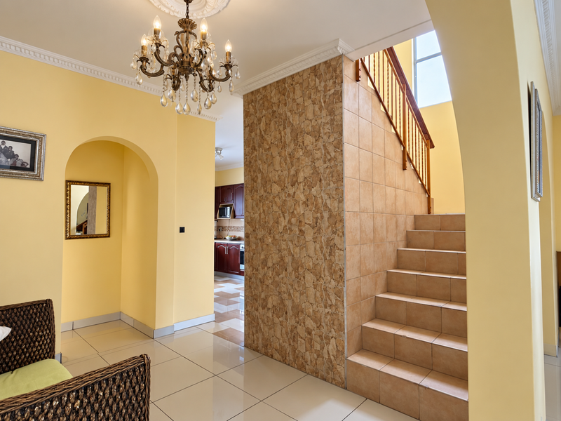 An inviting entrance hall featuring a tiled staircase with a wooden balustrade, a decorative stone-clad feature wall, and a classic chandelier.