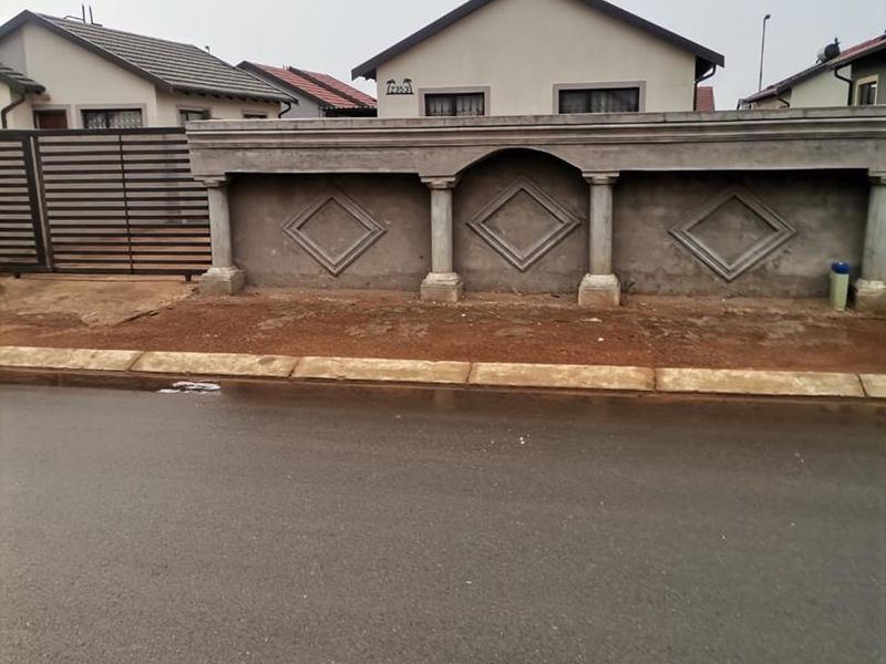 Street view of a residential property featuring a decorative perimeter wall with unfinished plaster and a metal driveway gate.