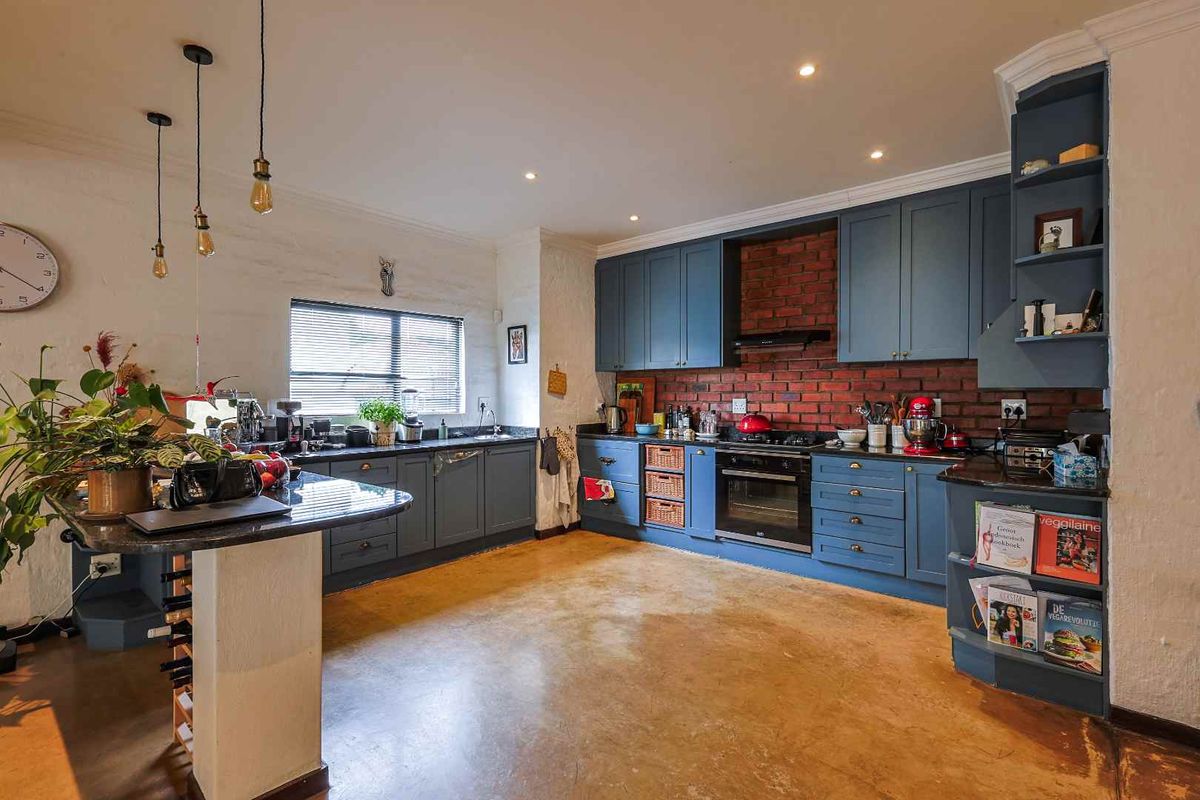 A well-appointed kitchen featuring blue cabinetry, a brick backsplash, polished concrete flooring, and a built-in oven with an extractor fan.