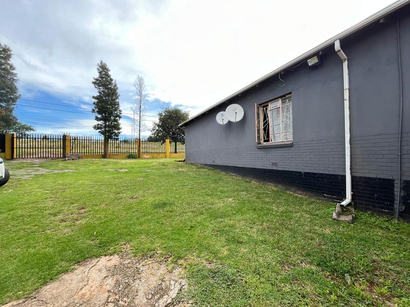 Rear view of the property featuring a painted brick exterior, security window bars, and a spacious lawn area enclosed by perimeter fencing.