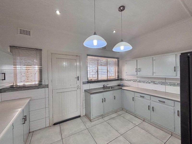 A functional kitchen featuring built-in cabinetry, tiled flooring, a stainless steel sink, and ample natural light through venetian blinds.