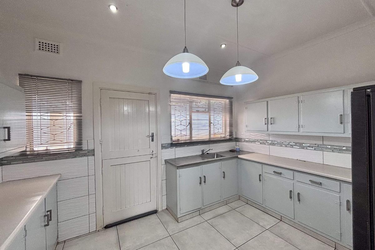A functional kitchen featuring built-in cabinetry, tiled flooring, a stainless steel sink, and ample natural light through venetian blinds.