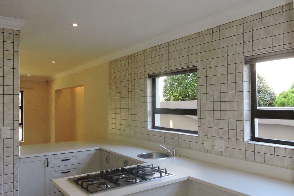 A clean, functional kitchen featuring a gas hob, stone countertops, tiled splashbacks, and ample built-in cabinetry with modern recessed lighting.