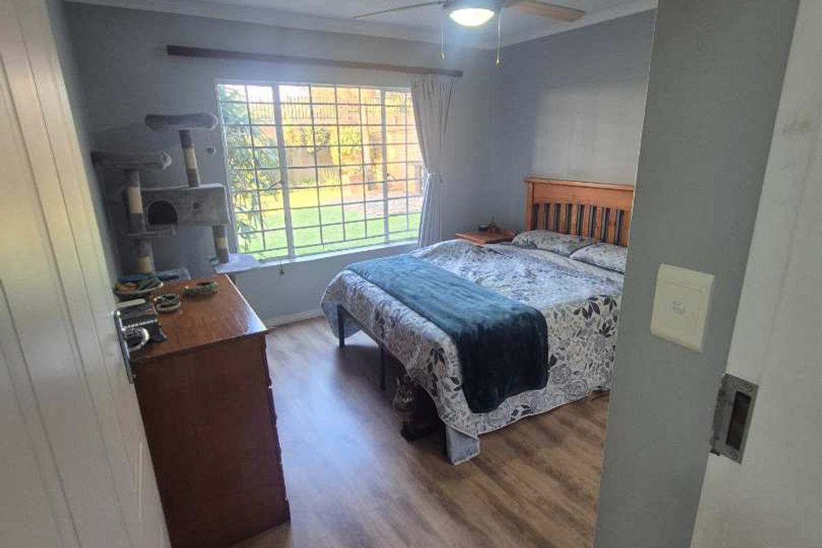 A bedroom featuring wood-look laminate flooring, a ceiling fan, and a large window providing natural light.