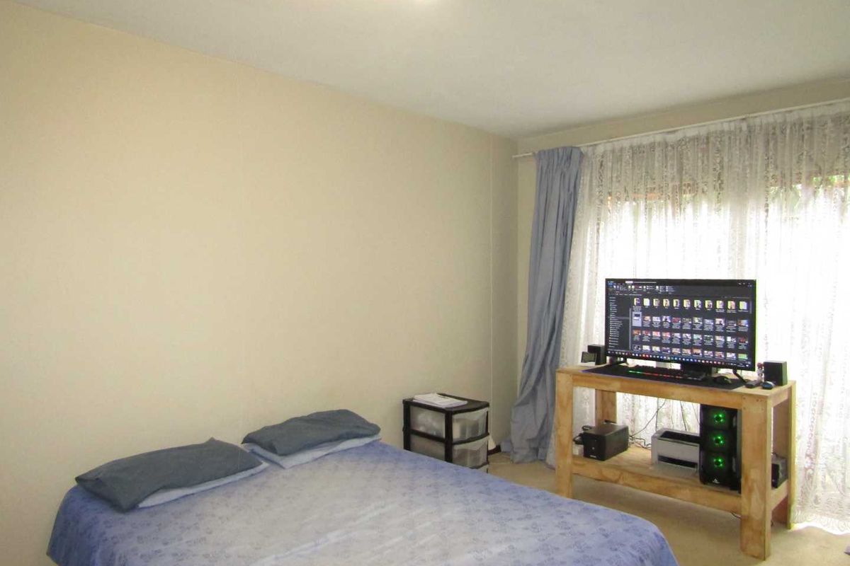 A bedroom featuring neutral wall tones, carpeted flooring, and a large window with curtains providing natural light.