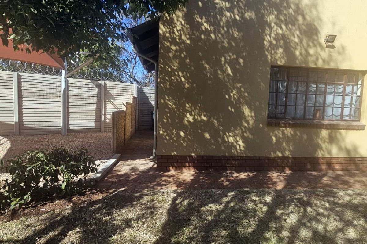 Rear exterior view of the property featuring a paved walkway, secure perimeter wall with razor wire, and established garden area.