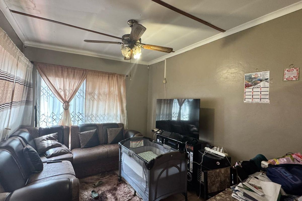 A living room featuring a ceiling fan and large windows with security gates, providing a functional space for relaxation.