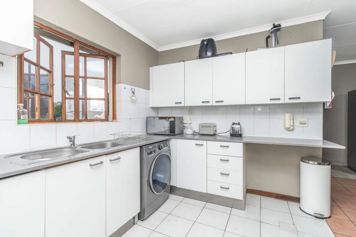 Functional kitchen featuring white cabinetry, stainless steel sink, tiled backsplash, and space for a washing machine under the counter.