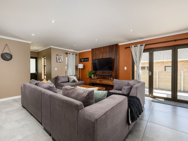 Spacious living room featuring modern tiled flooring, recessed downlights, and a stylish timber slat feature wall with direct access to the outdoor patio area.