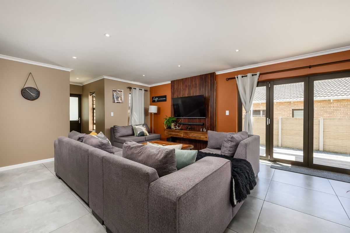 Spacious living room featuring modern tiled flooring, recessed downlights, and a stylish timber slat feature wall with direct access to the outdoor patio area.