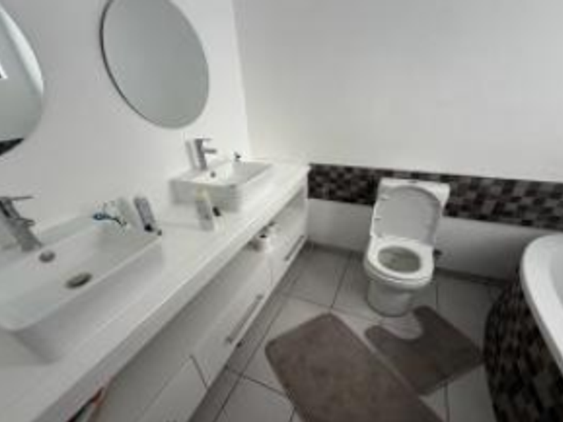 Modern bathroom featuring a double vanity with vessel sinks, chrome fixtures, a toilet, and a bathtub with decorative tiled accents.