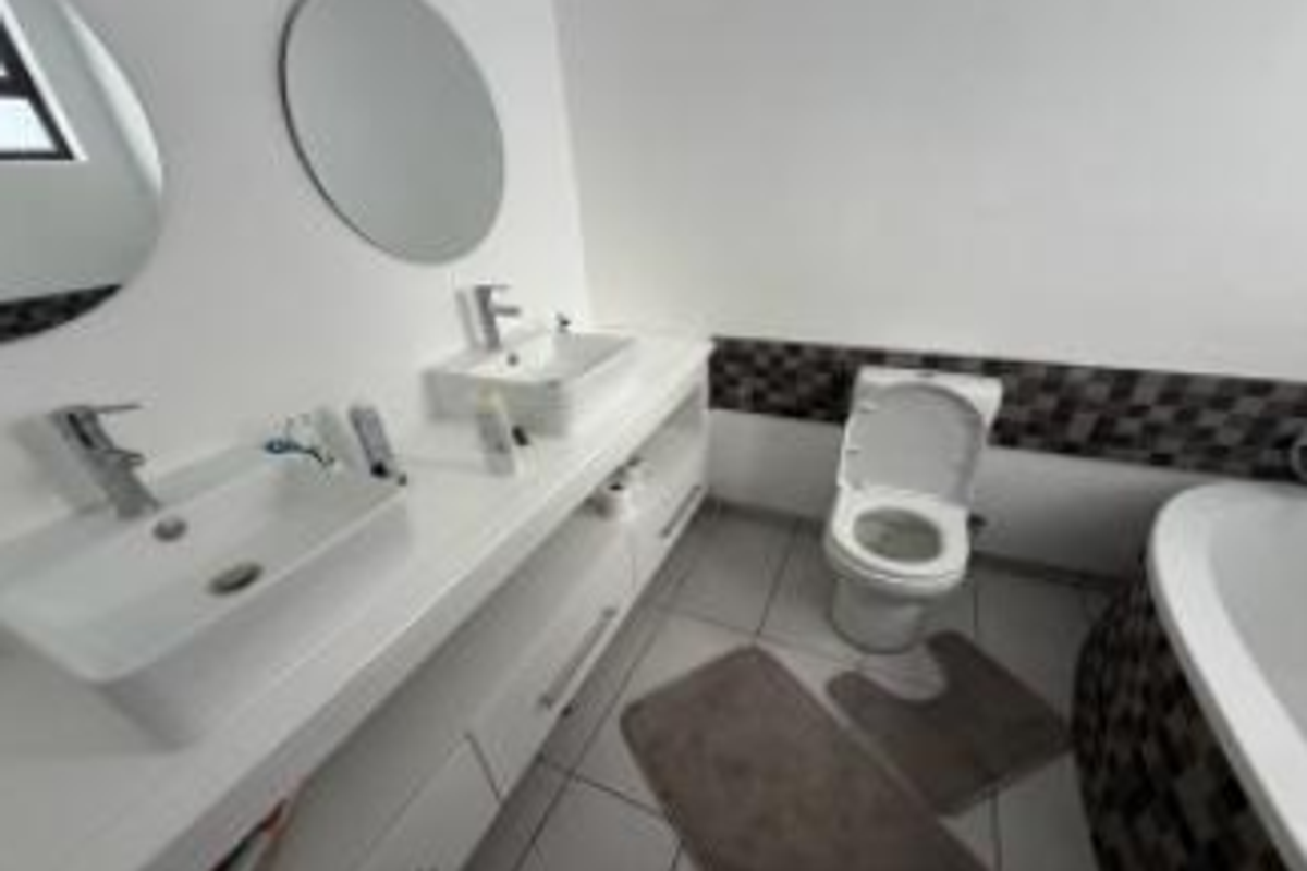 Modern bathroom featuring a double vanity with vessel sinks, chrome fixtures, a toilet, and a bathtub with decorative tiled accents.