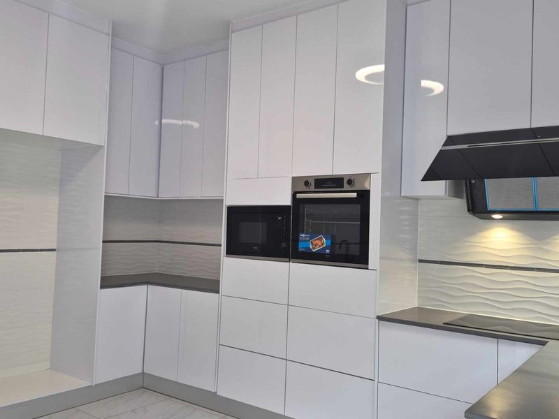Modern kitchen featuring high-gloss white cabinetry, integrated appliances including an oven and microwave, textured tile backsplash, and sleek stone countertops.