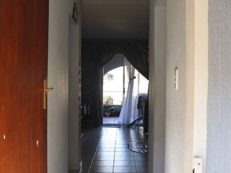 A functional apartment hallway featuring tiled flooring and a timber entrance door, leading through to an open-plan living area with balcony access.