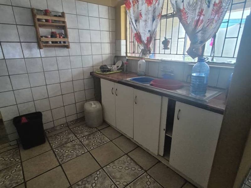A functional scullery area featuring built-in cabinetry, a stainless steel sink, and tiled finishes, requiring some maintenance and cosmetic updates.