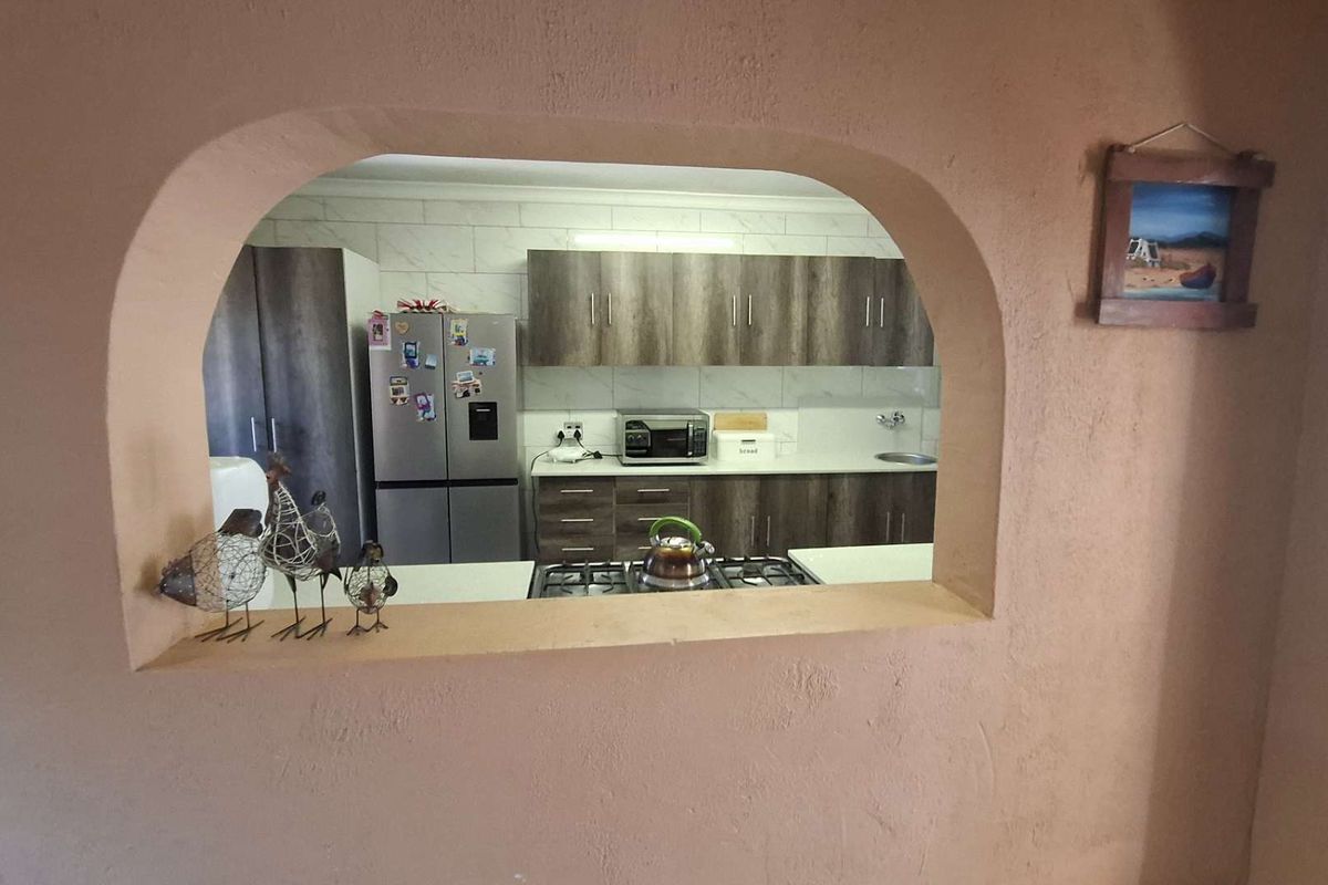 A kitchen viewed through a feature archway, featuring modern wood-look cabinetry, a gas hob, and tiled backsplash.