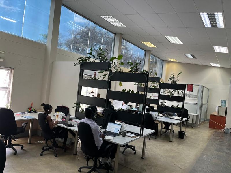 Spacious open-plan office area featuring high ceilings, large windows providing ample natural light, and modern partitioned workstations on concrete flooring.