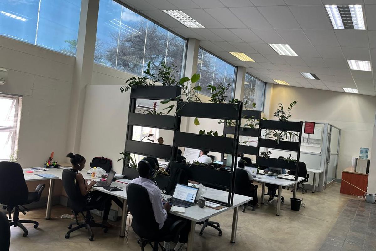 Spacious open-plan office area featuring high ceilings, large windows providing ample natural light, and modern partitioned workstations on concrete flooring.