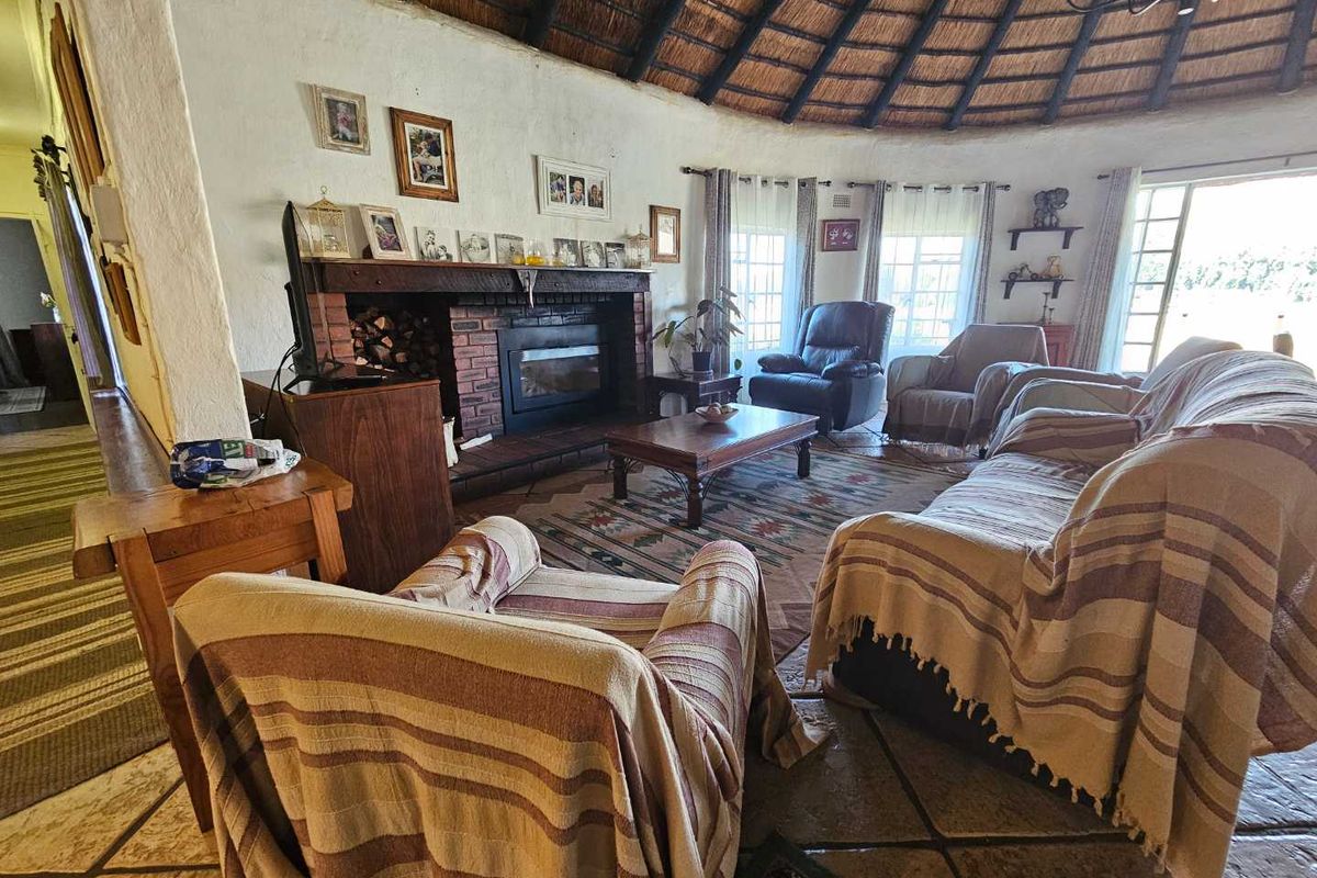 Spacious living room featuring a traditional thatched roof with exposed rafters, a brick fireplace, and stone tile flooring, offering a rustic farm-style atmosphere.