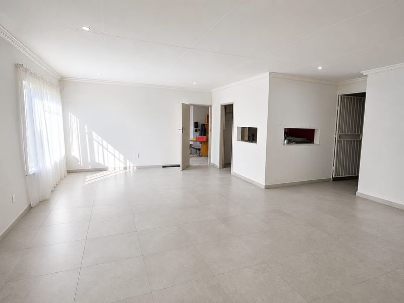 A bright, spacious, and empty living area featuring neutral tiled flooring, recessed ceiling lights, and decorative cornicing, offering a clean canvas for interior design.