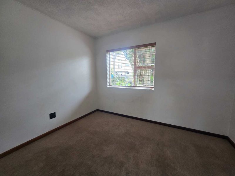 An empty bedroom featuring carpeted flooring, neutral walls, and a window with fitted blinds, offering a blank canvas for personalization.