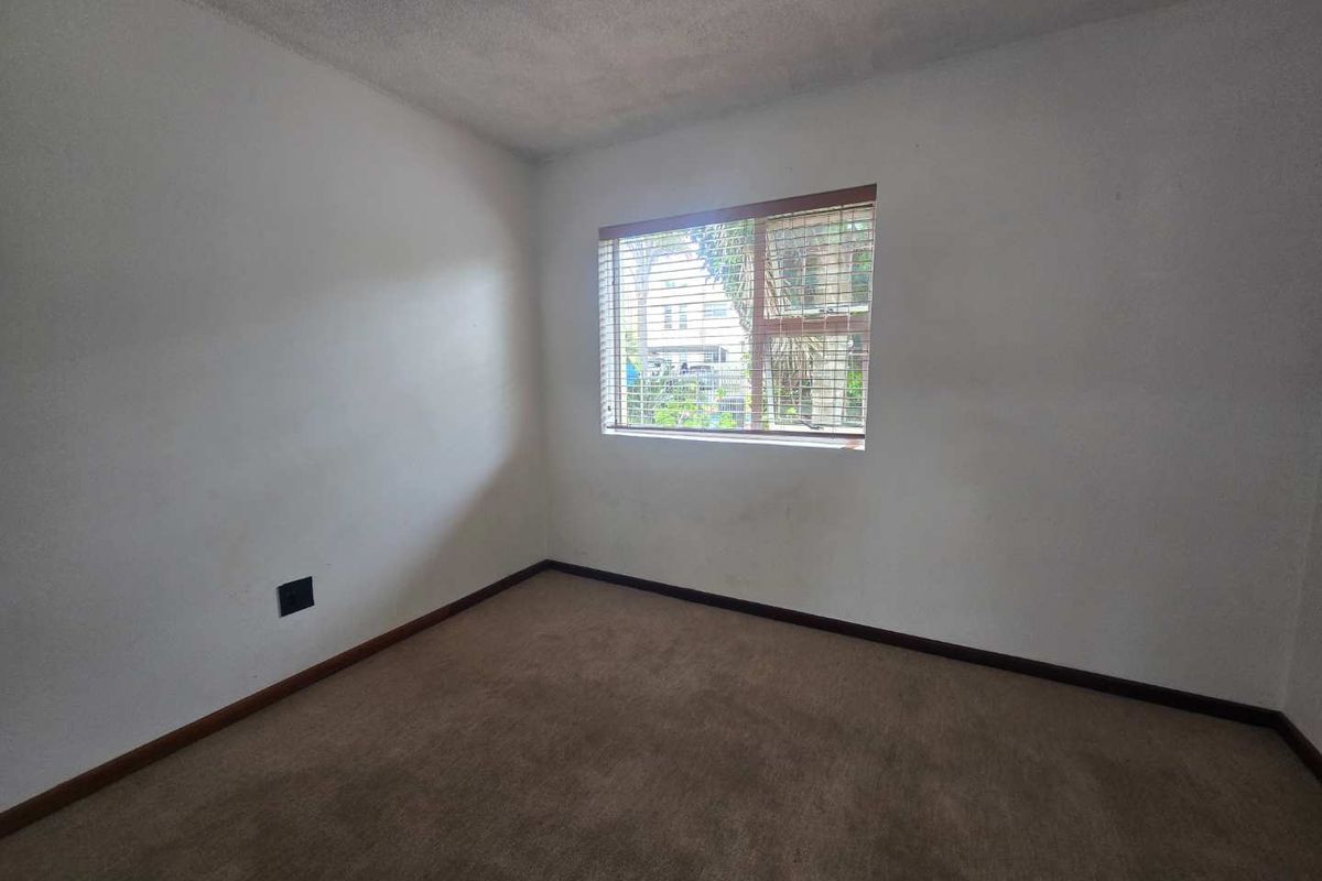 An empty bedroom featuring carpeted flooring, neutral walls, and a window with fitted blinds, offering a blank canvas for personalization.