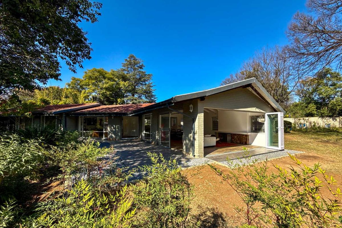 Rear view of the house featuring a paved patio area, bi-fold doors leading to the interior, and a well-established garden.