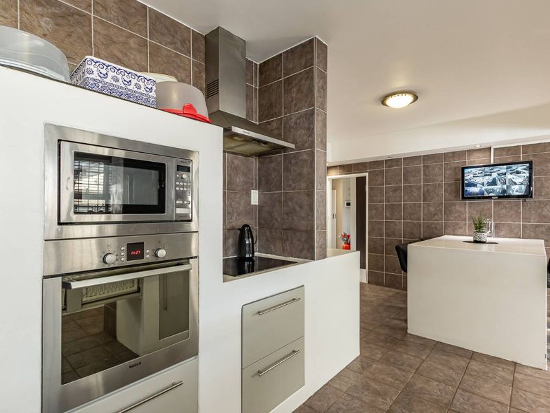 A functional kitchen featuring built-in stainless steel appliances, tiled splashbacks, and a central island, offering a practical layout for cooking and casual dining.