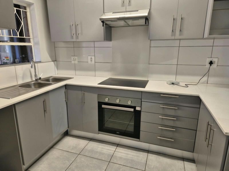Modern kitchen featuring grey built-in cabinetry, white countertops, tiled backsplash, and integrated appliances including an oven, hob, and extractor fan.