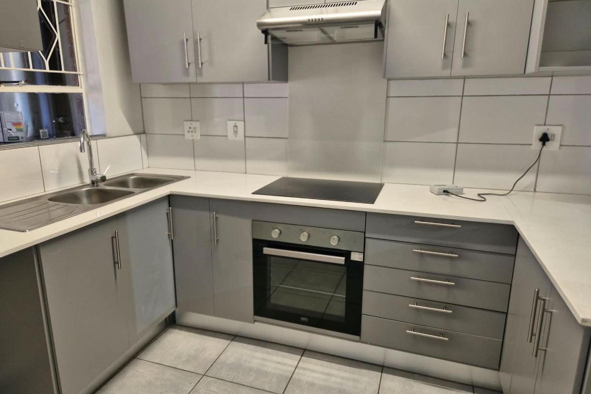 Modern kitchen featuring grey built-in cabinetry, white countertops, tiled backsplash, and integrated appliances including an oven, hob, and extractor fan.