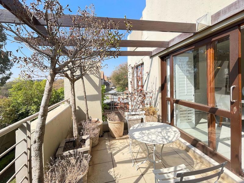 A sunny balcony featuring a timber pergola, tiled flooring, and sliding glass door access, offering an elevated outdoor space for relaxation.