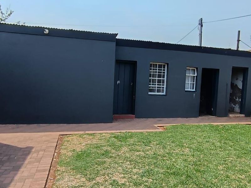 Rear exterior view of the property featuring a paved walkway, lawn area, and dark-painted exterior walls with security bars on windows.