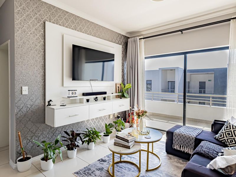A well-maintained living room featuring a built-in media console, decorative wallpaper, and large sliding glass doors leading to a private balcony.