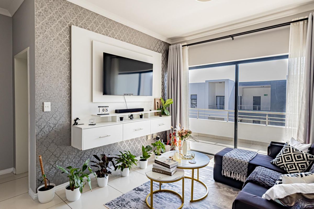 A well-maintained living room featuring a built-in media console, decorative wallpaper, and large sliding glass doors leading to a private balcony.