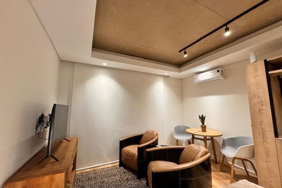 A modern living area featuring a recessed ceiling with track lighting, a wall-mounted air conditioning unit, and neutral finishes.