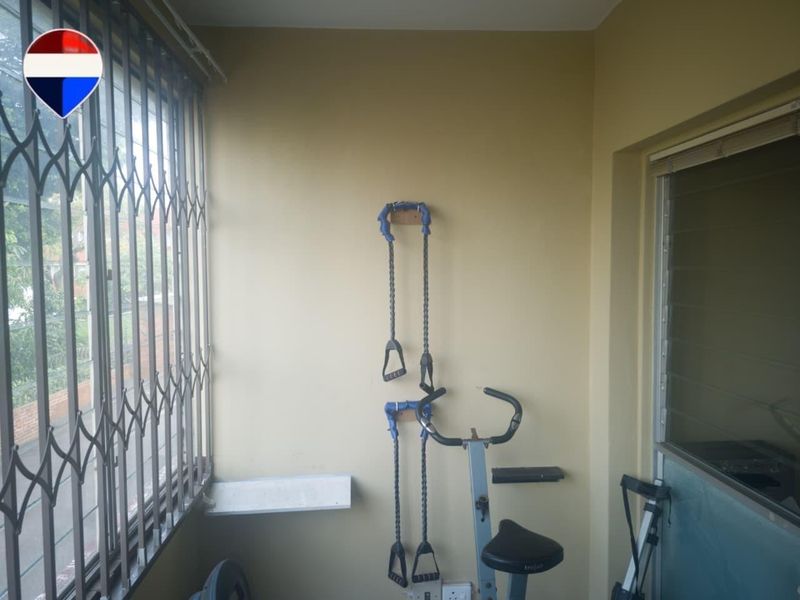 Enclosed balcony area featuring security gates and louvered windows, currently utilized as a home gym space.