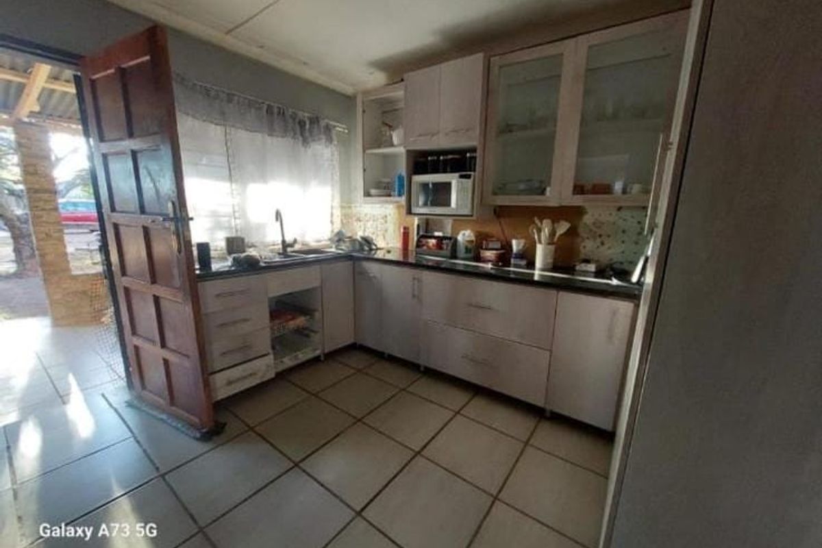 A functional kitchen featuring built-in cabinetry, laminate countertops, and tiled flooring, with direct access to an outdoor patio area.