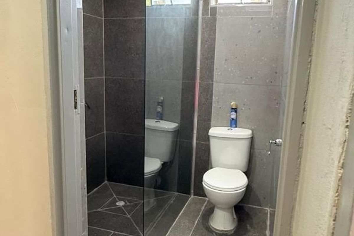 A compact bathroom featuring modern dark grey floor and wall tiles, a glass shower enclosure, and a standard toilet, currently awaiting final finishing touches.