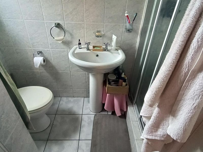 A functional bathroom featuring a pedestal washbasin, toilet, and a glass-enclosed shower with neutral ceramic wall and floor tiling.