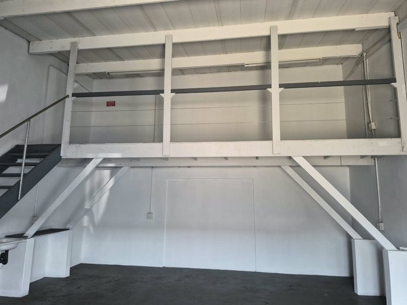 An industrial utility space featuring a mezzanine level with a staircase, exposed ceiling beams, and a functional wall-mounted sink.