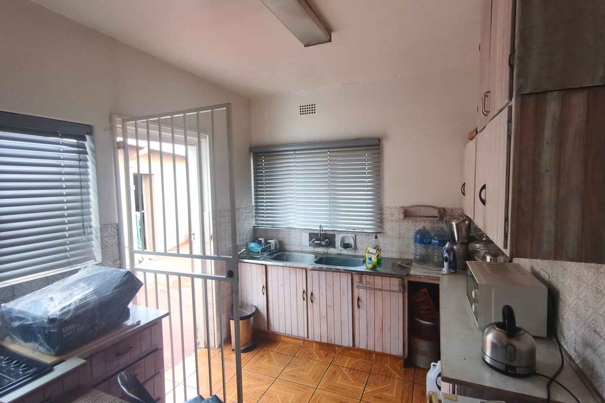 A functional kitchen featuring built-in cabinetry, a double sink, and tiled splashbacks, with direct access to an exterior area through a security gate.