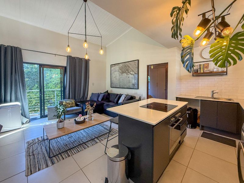 Modern open-plan living area featuring a kitchen island with built-in oven and hob, vaulted ceilings, and sliding glass doors leading to a balcony.