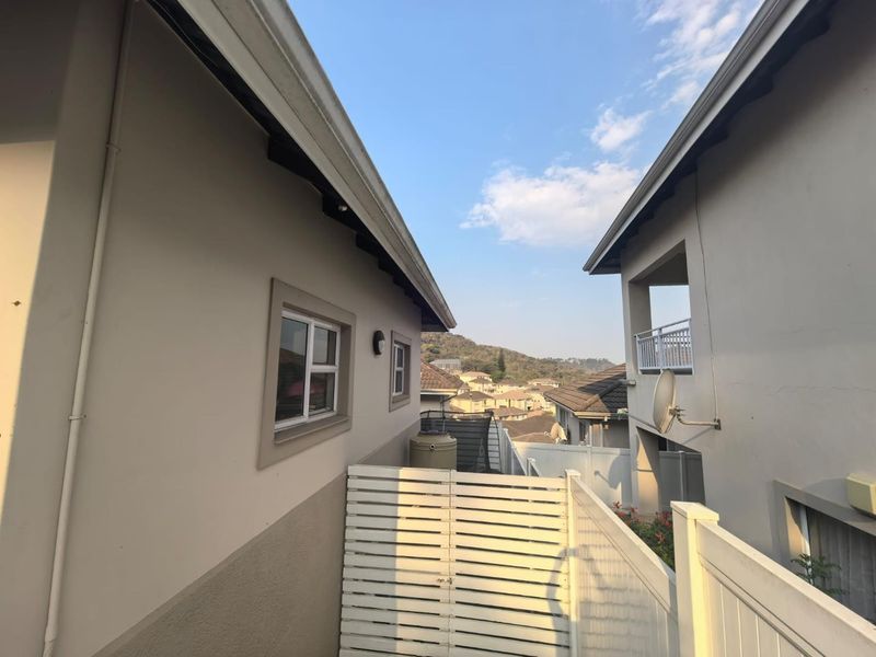 A view between two townhouse units showing the rear exterior space, including a water tank, satellite dish, and balcony overlooking the surrounding neighborhood.