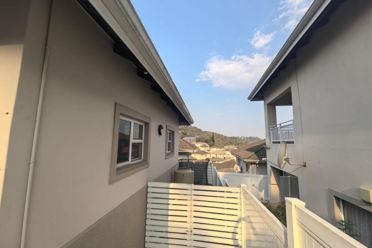 A view between two townhouse units showing the rear exterior space, including a water tank, satellite dish, and balcony overlooking the surrounding neighborhood.
