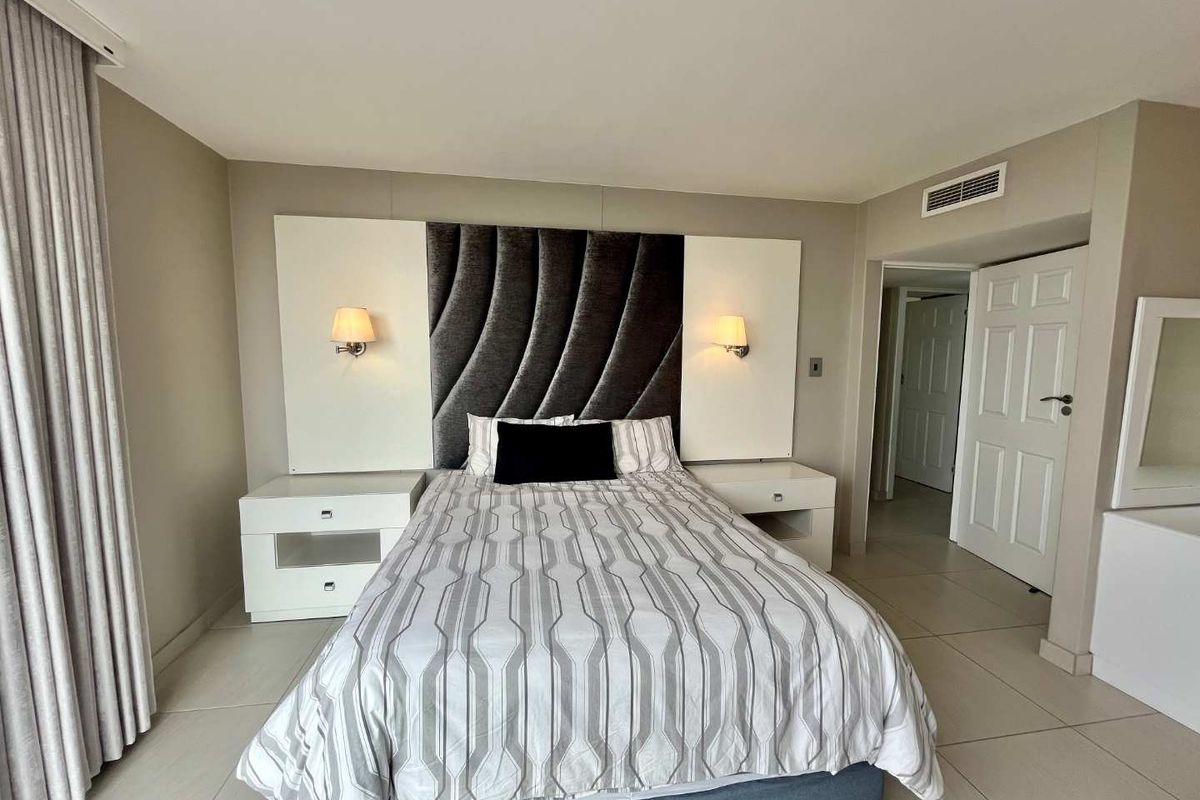 A well-maintained bedroom featuring a built-in headboard with integrated lighting, tiled flooring, and ducted air conditioning.