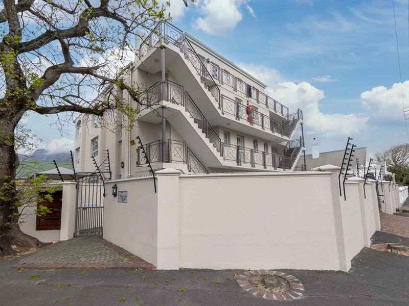 Exterior view of a multi-story apartment building featuring a secure perimeter wall with electric fencing and external stair access.