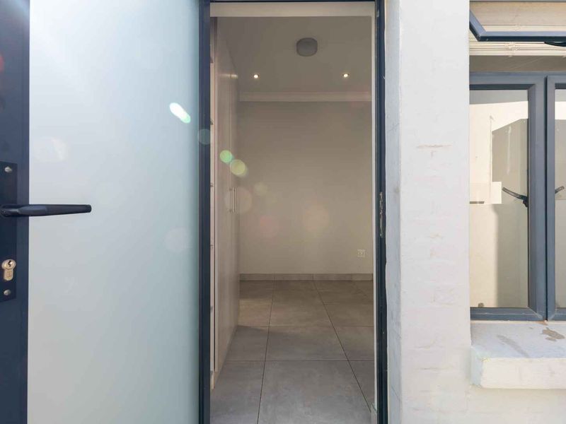 A view through an open doorway into a clean, empty bedroom featuring tiled floors, built-in cupboards, and modern recessed lighting.